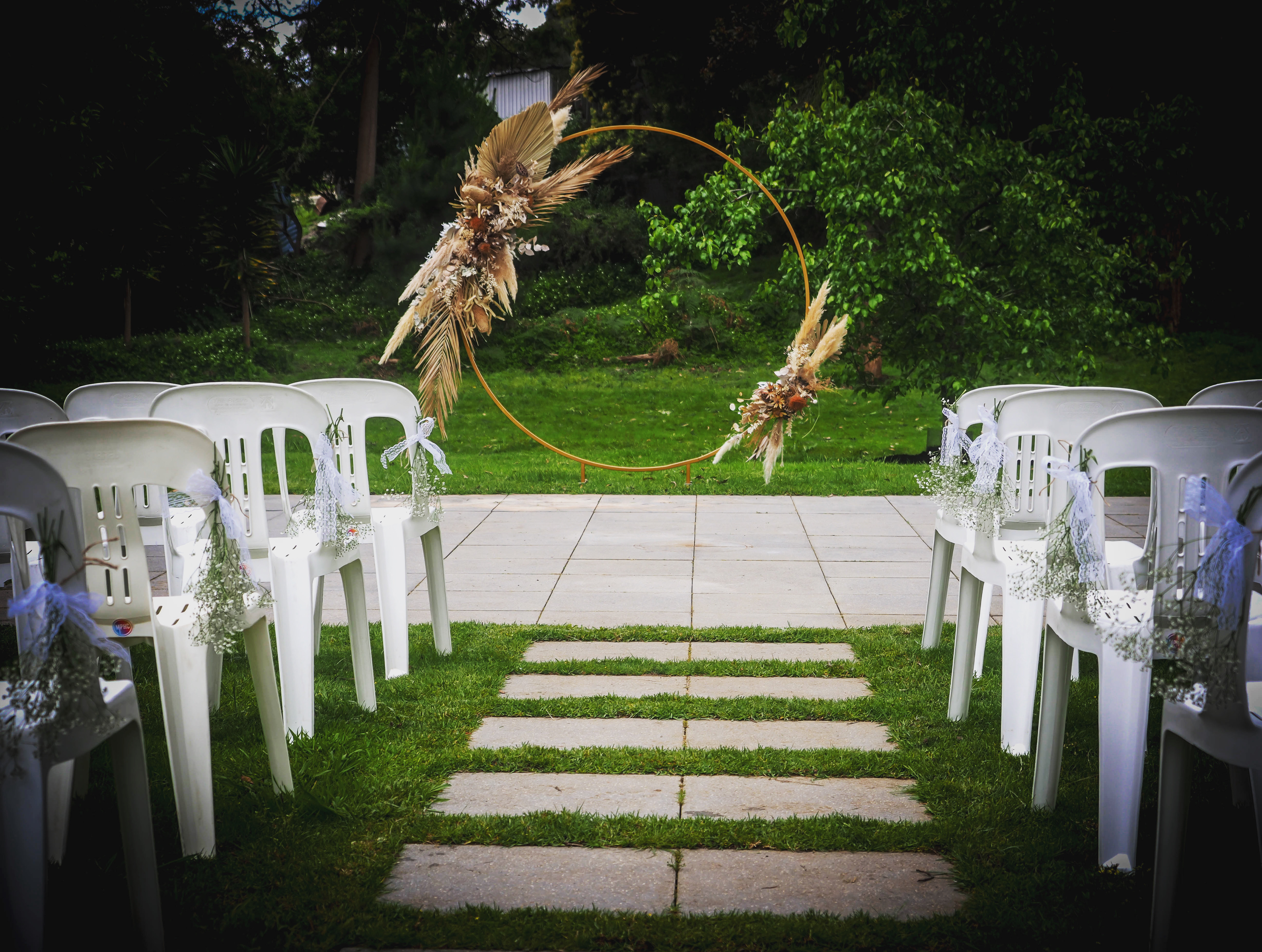 Golden arbour with dried flowers on a lawn with white chairs
